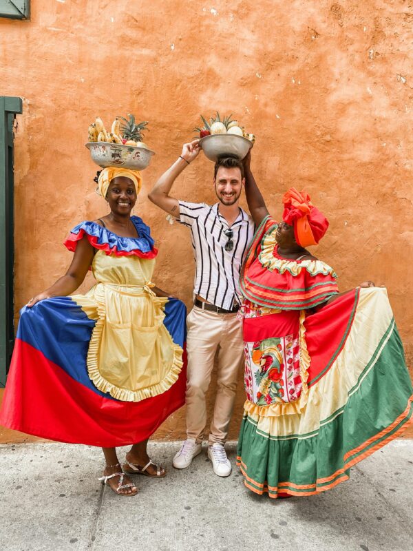 Colorful traditional dress and fruit vendors pose with a tourist in Cartagena, Colombia.